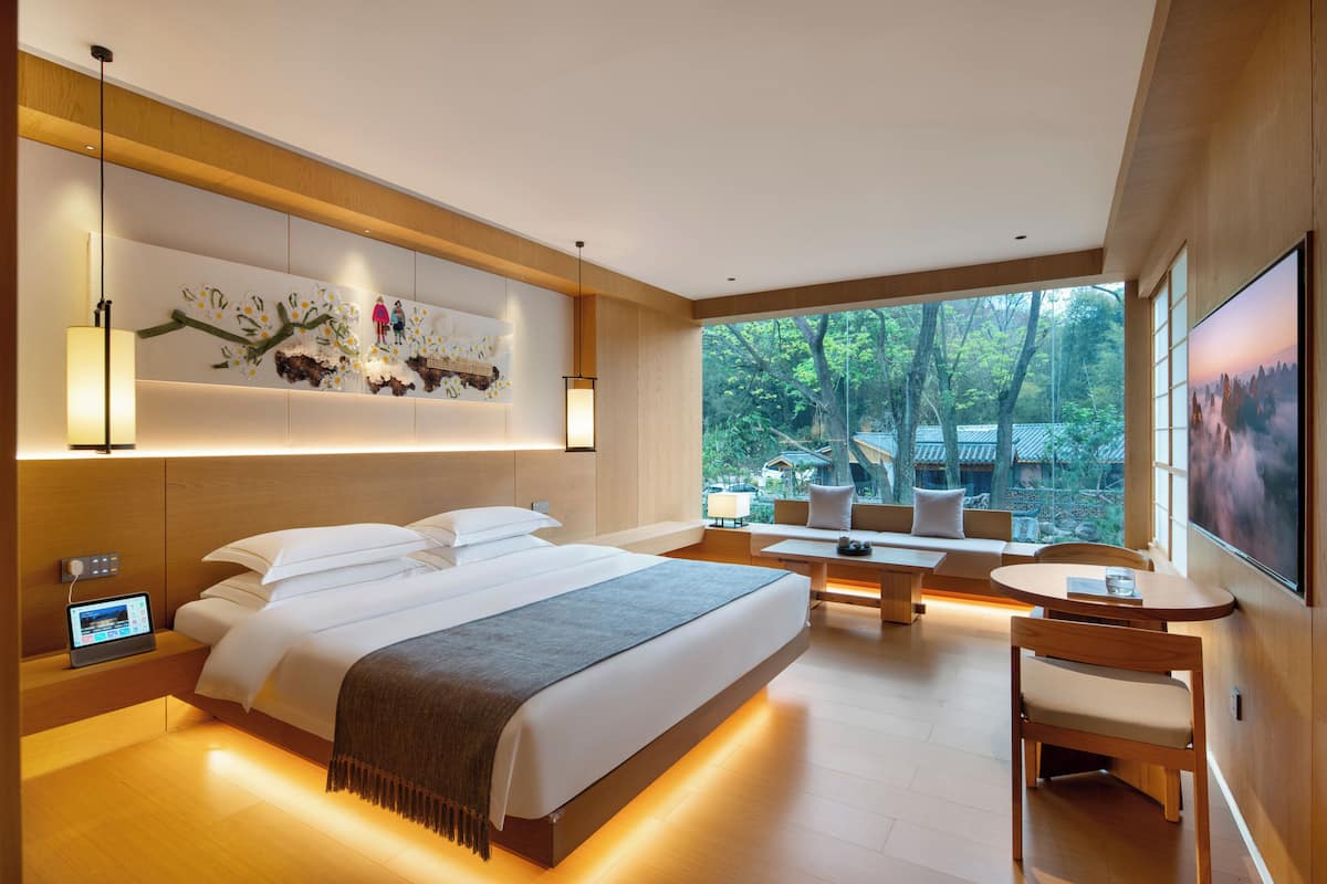 Una habitación de hotel moderna con una cama grande, un escritorio y vistas a árboles.