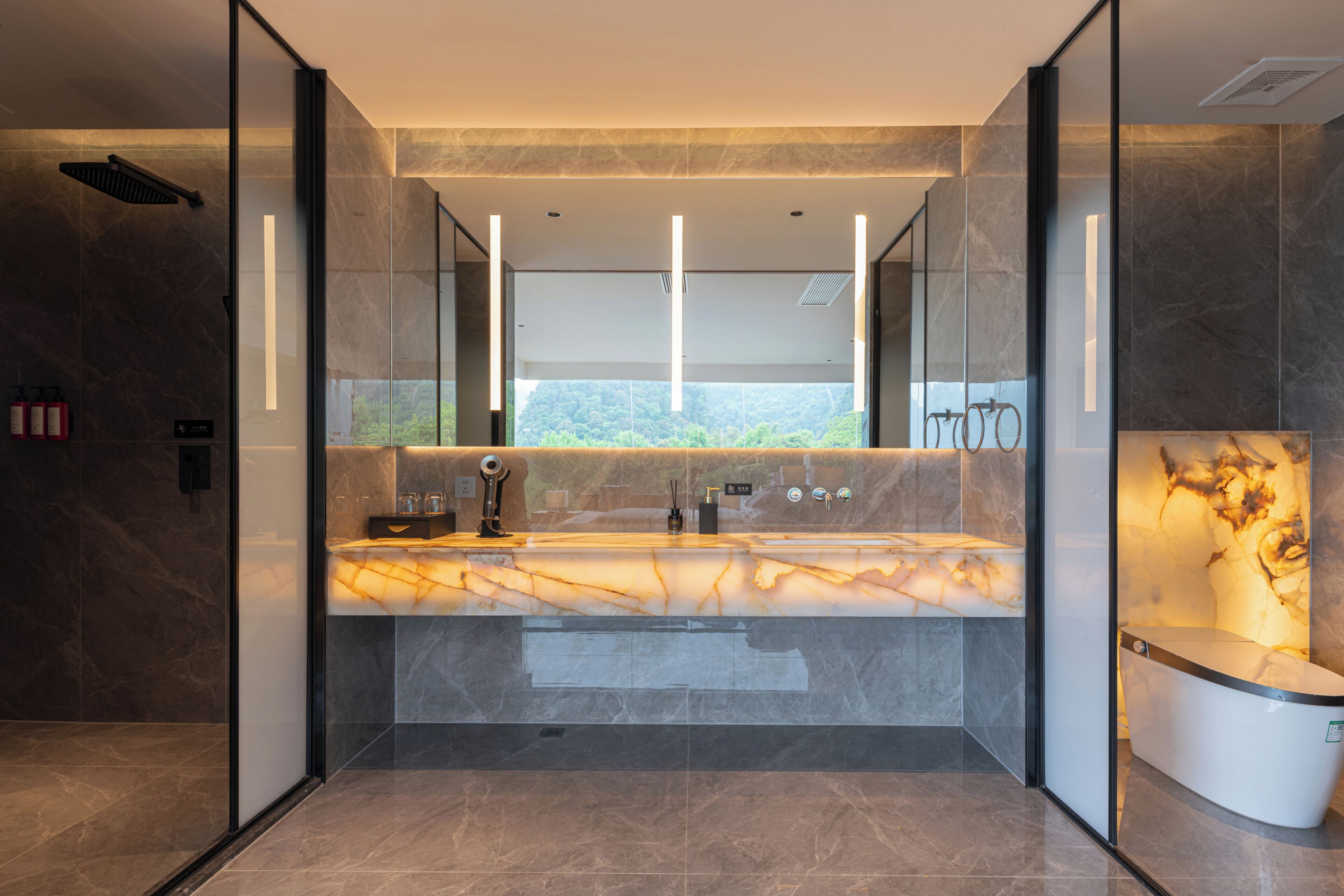 Un baño moderno con tocador de mármol, cabina de ducha de vidrio y vistas al exterior.