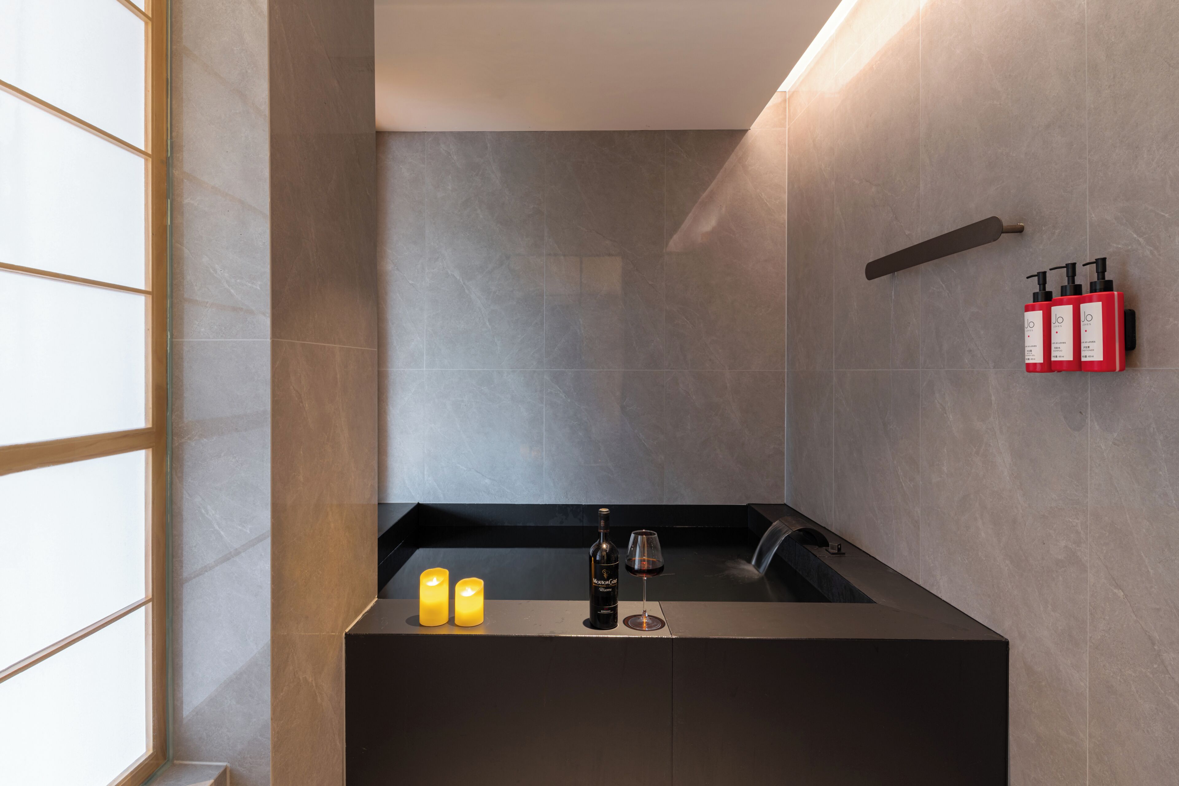 A modern bathroom with a bathtub, candles, a wine bottle, and toiletries.