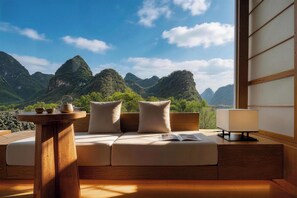 A room with a sofa facing a mountain view, a small table with a lamp, and a window with traditional sliding doors. - Wushan Chujian Homestay (Guilin)