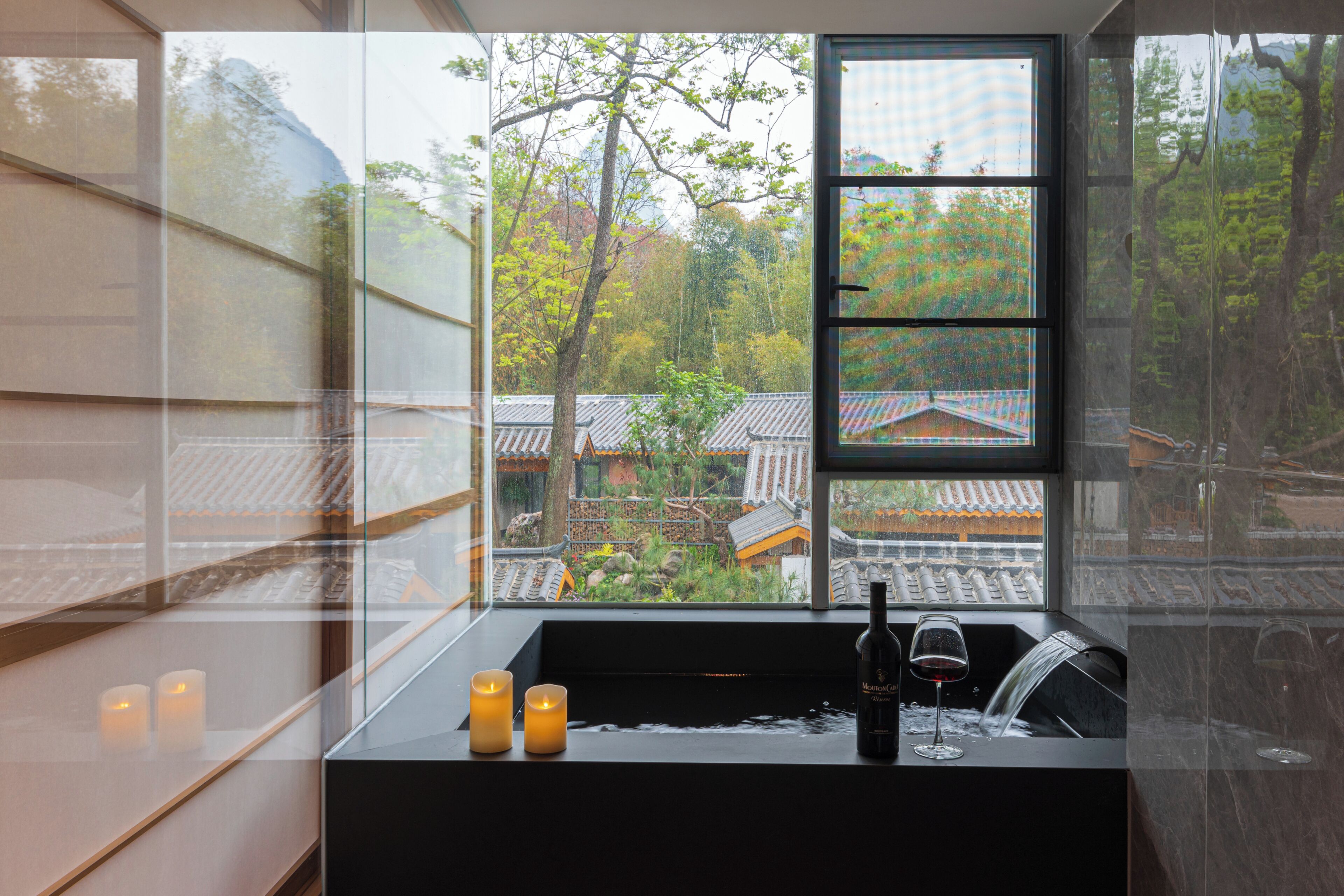 A bathroom with a window, candles, a wine bottle, and a sink.