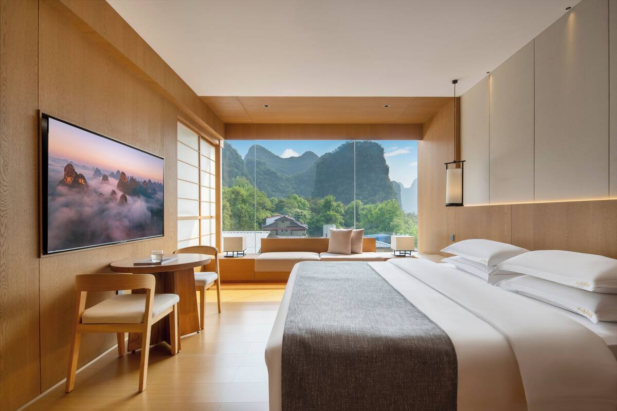 Habitación de hotel moderna con una cama grande, televisor, escritorio con silla y vistas a montañas.