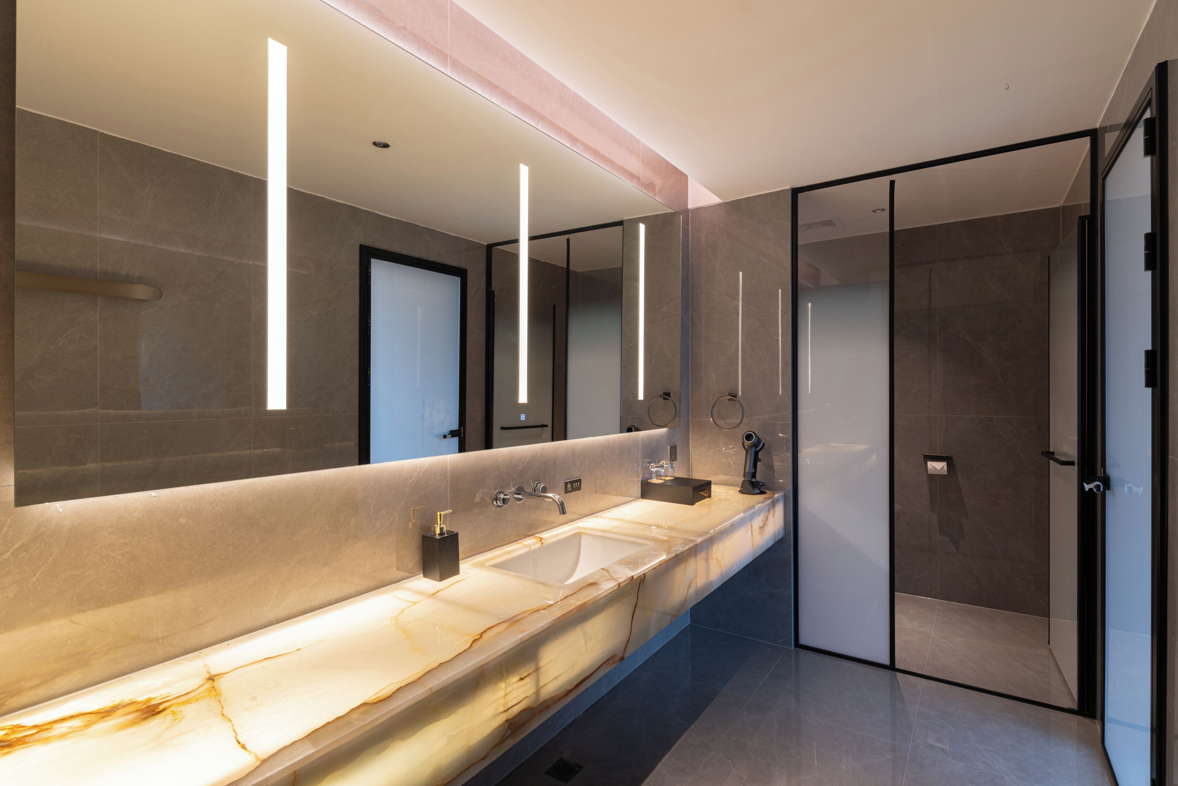 A modern bathroom with a marble sink, a large mirror, and a glass shower enclosure.