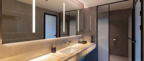 A modern bathroom with a marble sink, a large mirror, and a glass shower enclosure.