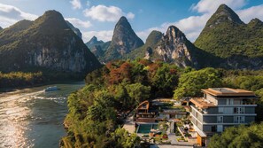 A coastal hotel with a swimming pool, a boat on the water, and mountainous terrain in the background. - Wushan Chujian Homestay (Guilin)