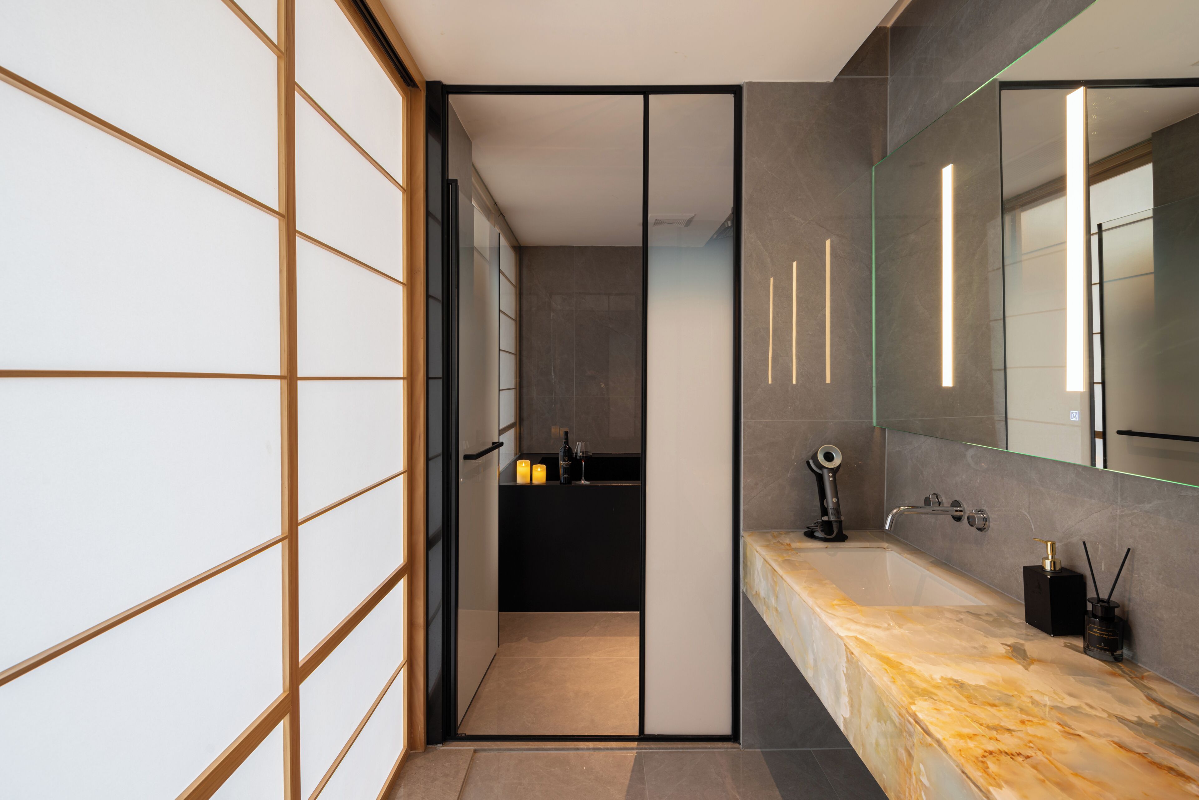 Un baño moderno con separador de vidrio, encimera de mármol y un espejo grande.