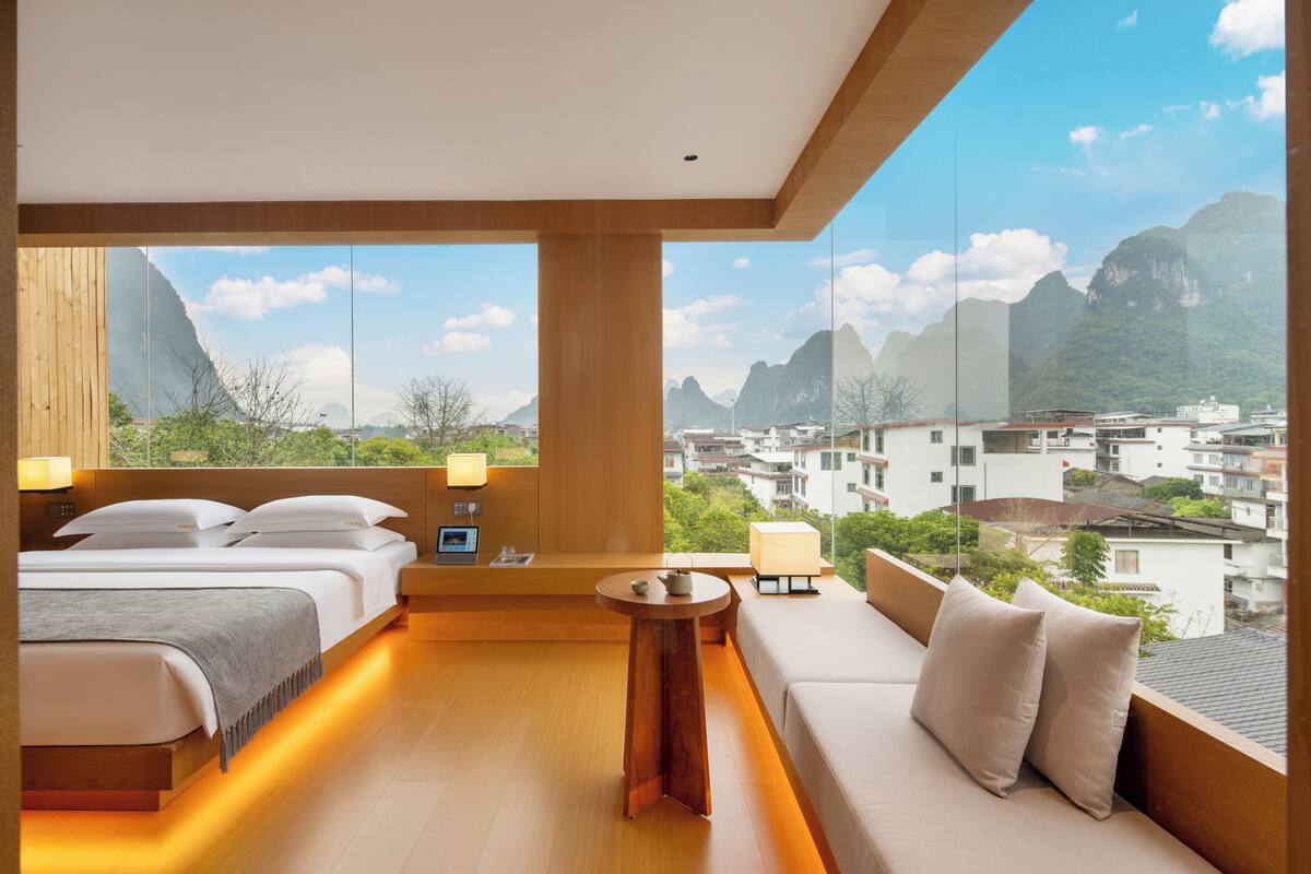 Habitación de hotel con cama, sofá, una mesita y vistas a la ciudad y las montañas.