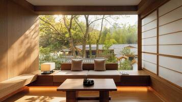 A traditional Japanese room with tatami flooring, a low table with tea set, a cushioned bench, and a view of traditional houses through a shoji screen.