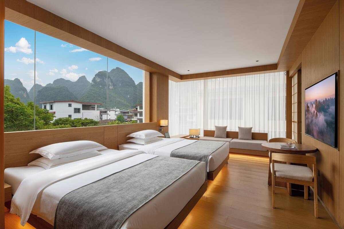 Habitación de hotel con dos camas, zona de estar, televisión y vistas a las montañas.