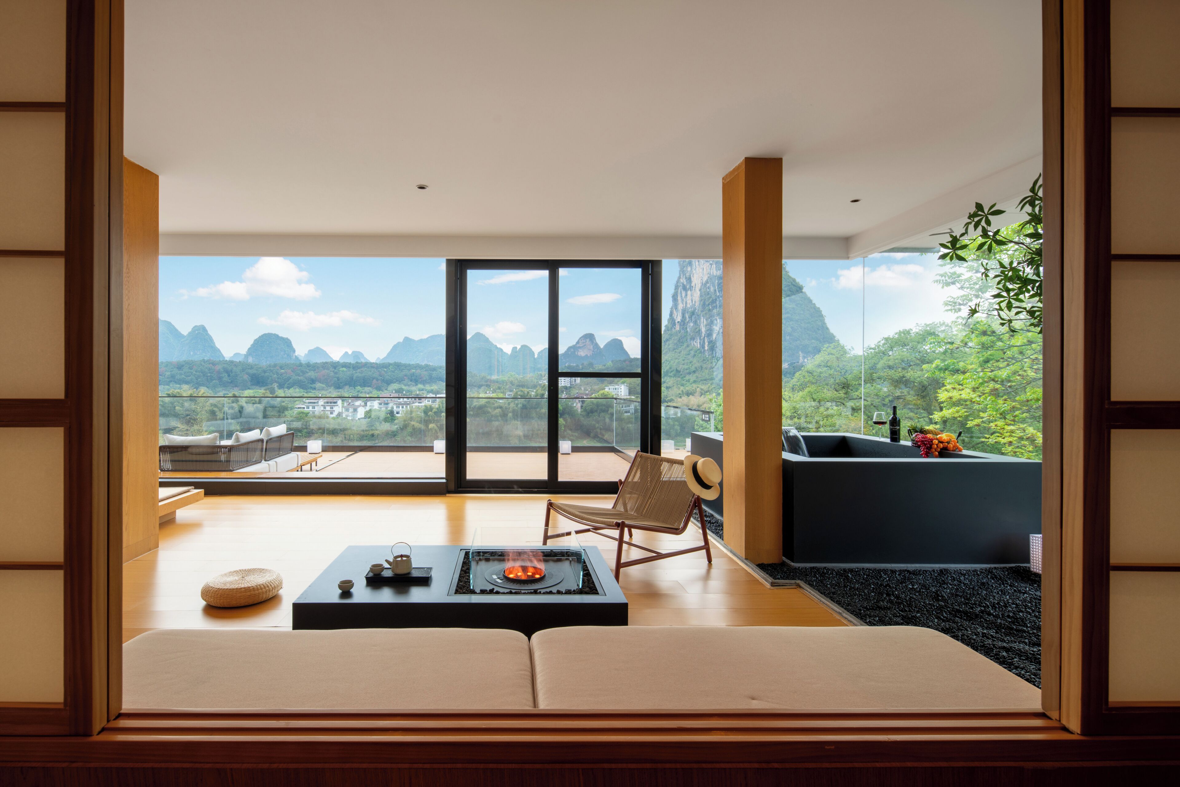 A modern interior with a large window, a sofa, a chair, and a small table with a fire feature.