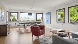 A spacious living area with a dining table, chairs, a red armchair, a grey sofa, and large windows offering views of greenery. - 3 bedroom stunning home in Varberg (Varberg)