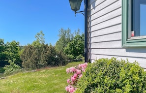 Un bâtiment blanc avec un cadre de fenêtre vert, un lampadaire noir et une haie ornée de fleurs roses.