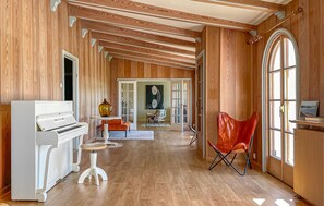 Ein geräumiger Raum mit Holzwänden, einem Klavier, einem roten Sessel und einem großen Fenster.