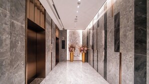 Un pasillo moderno con suelo de mármol, un arreglo floral central y un ascensor empotrado en la pared.