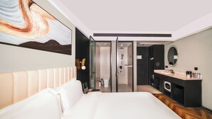 Una habitación de hotel moderna con una cama grande, un baño con ducha, un tocador con espejo y un cuadro en la pared.