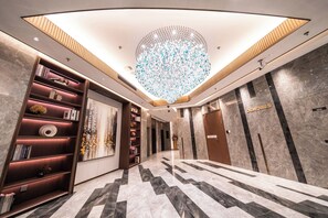 Eine moderne Hotelhalle mit einer großen Chandelier, Marmorböden und einer Bücherwand mit Dekorationselementen.