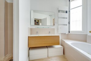 Een moderne badkamer met een witte wastafel, een spiegel, een badkuip en een raam.