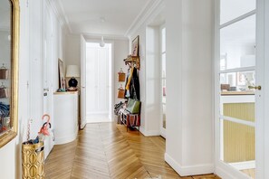 Ein Gang mit Holzboden, weißen Wänden, einer Tür am Ende und einem Fenster rechts.