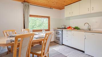 Cuina moderna amb armaris blancs, forn integrat i menjador amb caires de fusta i taula per a dues persones.