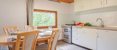 A modern kitchen with white cabinets, a built-in oven, and a dining area with wooden chairs and a table set for two.