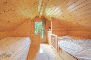 A wooden cabin with two beds, a window, and a view of the forest. - Hideaway Lodge Trtinka (Zalec)
