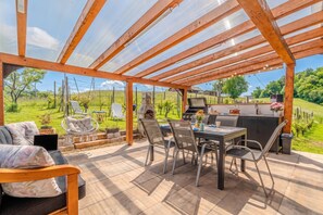 Eine überdachte Terrasse mit Tisch, Stühlen, einem Grill und einem Hängesessel.