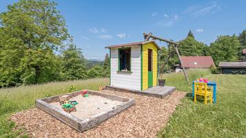 A small playhouse with a colorful exterior, a sandbox with toys, and a wooden swing set.