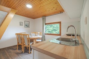 A kitchen with a wooden ceiling, a dining table with chairs, a window with a view, and a sink. - Hideaway Lodge Trtinka (Zalec)