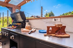 Cuina exterior amb una graella, una taula de tallar, un ganivet i una barra de pa.