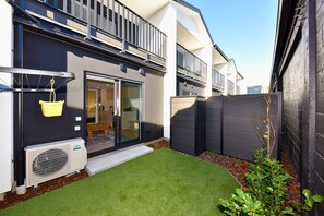 A modern house with a sliding glass door entrance, a small patio with artificial grass, and a black fence. - Stylish 1BR Stay on Moorhouse Avenue (Christchurch)