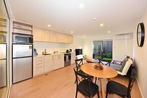 A modern kitchen with a built-in oven, microwave, and refrigerator. There is a dining area with a round table and chairs, and a sofa with a view of the outdoors. - Stylish 1BR Stay on Moorhouse Avenue (Christchurch)