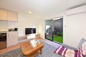 A modern living room with a flat-screen TV, a wooden coffee table, a sofa, and a sliding glass door leading to a garden. - Stylish 1BR Stay on Moorhouse Avenue (Christchurch)