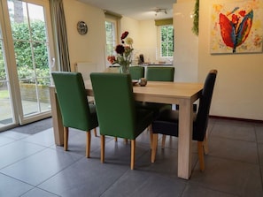A dining area with a table and chairs, a clock on the wall, and a window with a view of greenery. - Villa in Beekbergen With Terrace (Beekbergen)