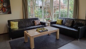 Sala de estar con dos sofás de cuero negro, una mesa de centro de madera y ventanas amplias con cortinas.