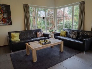 A living room with two black leather sofas, a wooden coffee table, and large windows with curtains. - Villa in Beekbergen With Terrace (Beekbergen)