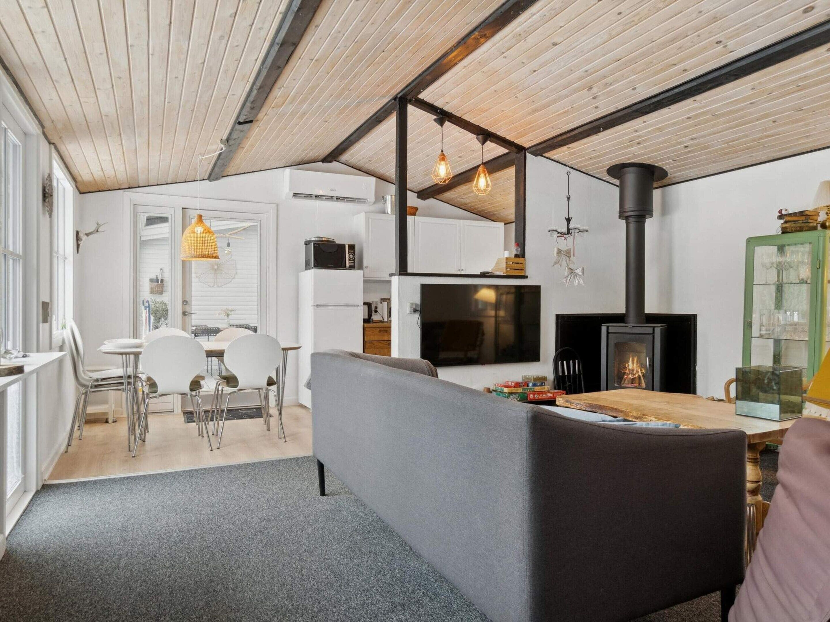 Cozinha moderna com armários brancos, fogão preto e uma área de jantar com sofá cinza e mesa de madeira.