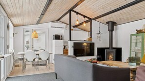 A modern kitchen with white cabinets, a black stove, and a dining area with a gray sofa and a wooden table. - 4 Star Holiday Home in Nakskov (Nakskov)