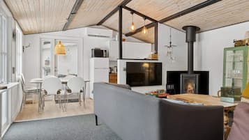 Cozinha moderna com armários brancos, fogão preto e uma área de jantar com sofá cinza e mesa de madeira.