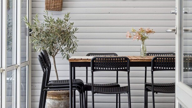 A dining area with a table, chairs, a potted plant, a vase with flowers, a wall-mounted basket, and a decorative fan. - 4 Star Holiday Home in Nakskov (Nakskov)