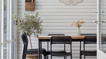 Uma área de refeições com uma mesa, cadeiras, um vaso de plantas, um vaso com flores, uma cesta fixada na parede e um leque decorativo.
