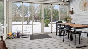 A covered patio with a wooden table and chairs, large sliding glass doors, and a view of a snowy yard. - 4 Star Holiday Home in Nakskov (Nakskov)