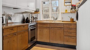 A kitchen with wooden cabinets, a stove, a coffee maker, and a window with a view of trees. - 4 Star Holiday Home in Nakskov (Nakskov)