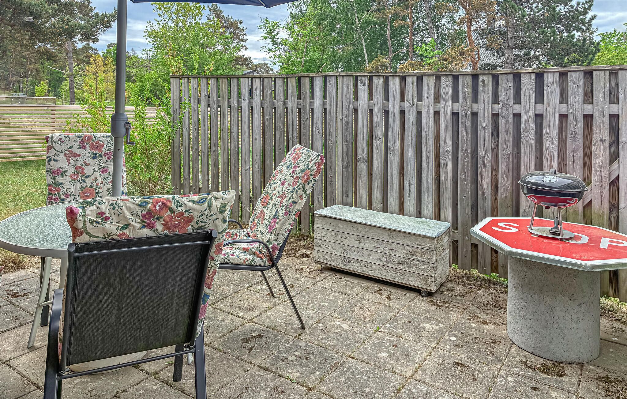 An outdoor patio with a round table, two chairs with floral cushions, a bench, and a barbecue grill.