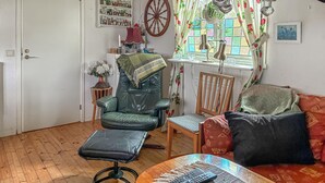 Un salon chaleureux avec un fauteuil en cuir, une chaise en bois, une petite table avec une télécommande et une fenêtre agrémentée de rideaux colorés.