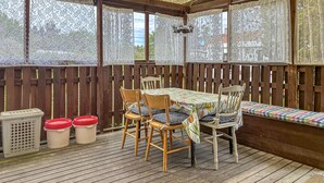 Une terrasse couverte avec une table et des chaises en bois, un banc et une vue à travers des rideaux en dentelle.
