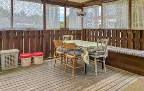A covered patio with a wooden table and chairs, a bench, and a view through lace curtains. - Awesome home in Vibble with WiFi (Vibble)