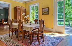 Ein Esszimmer mit Tisch, gedeckt für vier Personen, umgeben von Holzstühlen, einem großen Holzschrank und einer Vase mit Blumen.