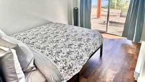 Une chambre à coucher avec un lit, une vue sur l’extérieur grâce à une porte coulissante et une fenêtre avec des rideaux.