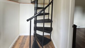 Un escalier en colimaçon avec une rampe en métal, un plancher en bois et une plante en pot sur la plateforme.