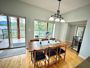 Un'area pranzo con tavolo e sedie in legno, ampie finestre con vista sul verde e un balcone con ringhiera.